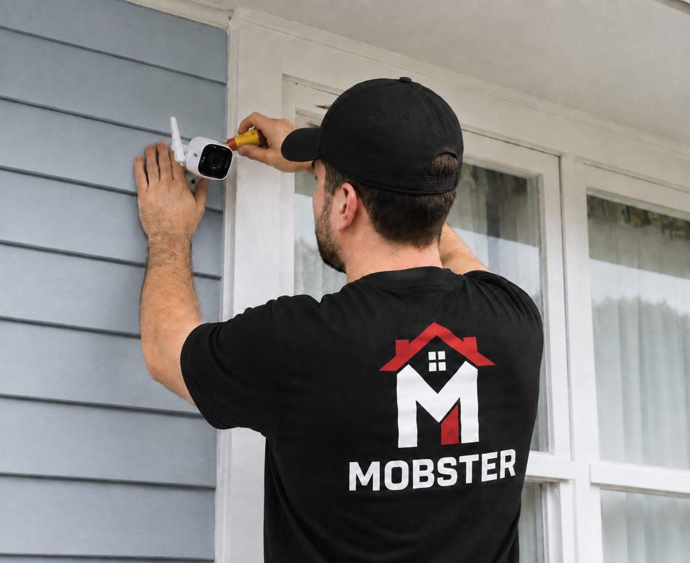 A Mobster fixing an outdoor security camera to the siding beside a window