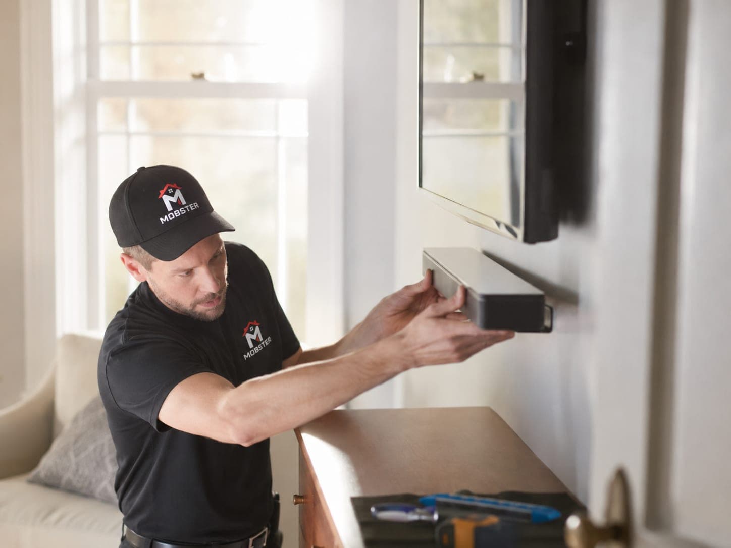 A Mobster fitting a soundbar to the wall beneath a mounted television