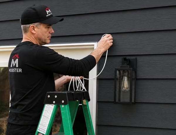 A Mobster fitting an outdoor wall light beside a doorway